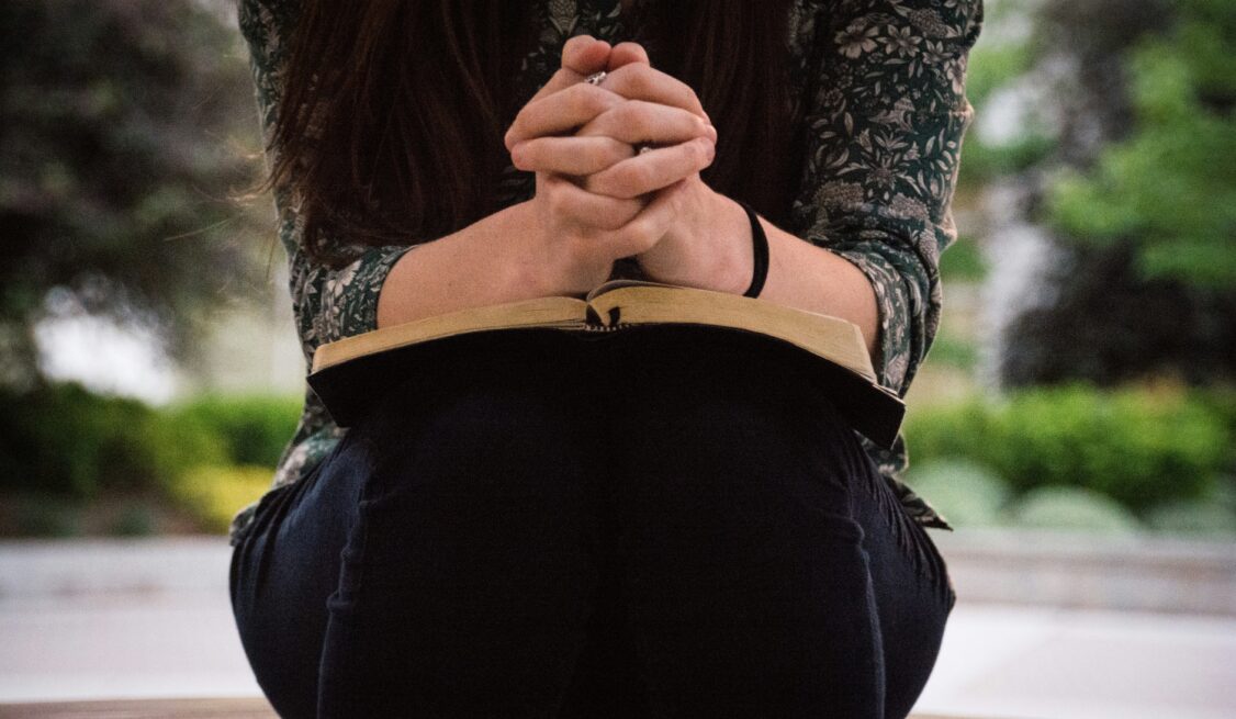 Prayinh with hands clasped over a Bible