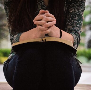 Prayinh with hands clasped over a Bible
