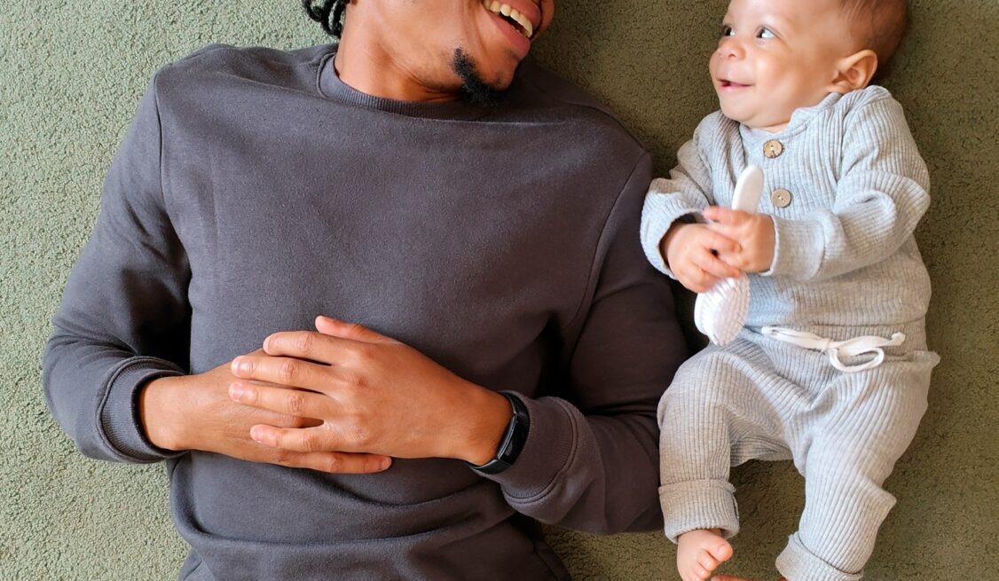 A black man and a white newborn infant smiling at each other