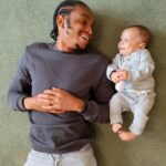 A black man and a white newborn infant smiling at each other