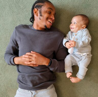 A black man and a white newborn infant smiling at each other